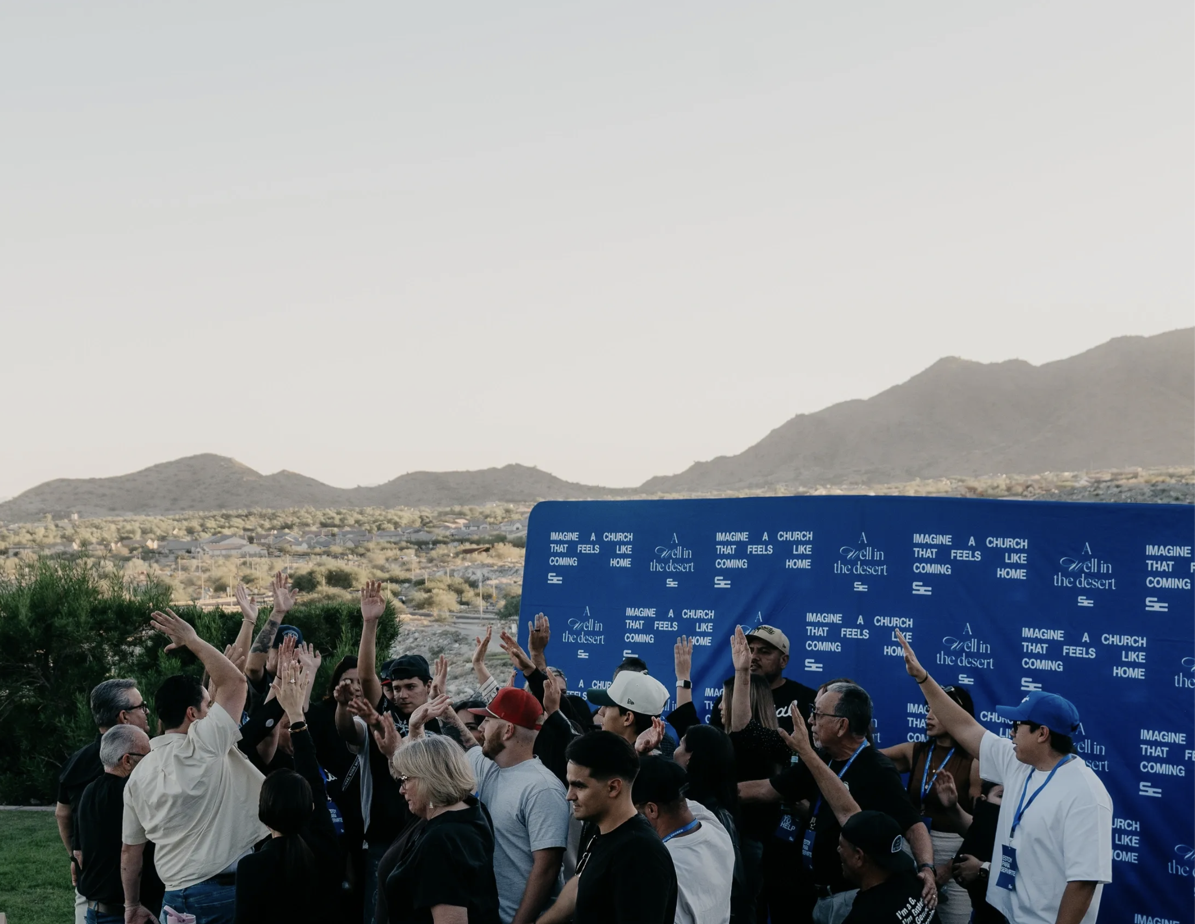 The Social Church community gathered outdoors with raised hands and desert mountains behind them.